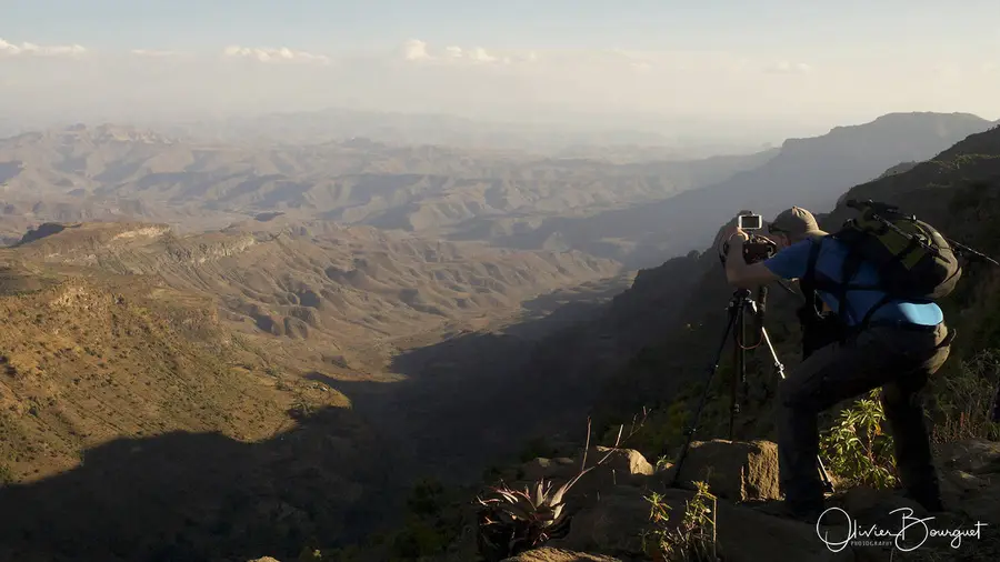 Un photographe et son trépied au bord d’un escarpement, face aux montagnes d’Éthiopie