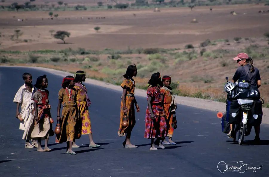 Des jeunes filles en robes colorées sur la route, à côté d’une cycliste chargée, en Éthiopie