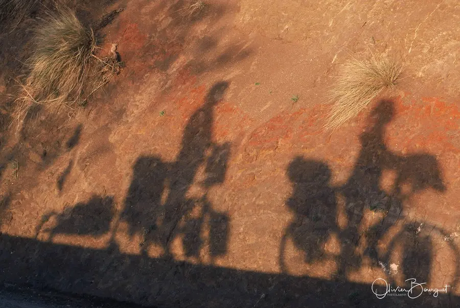 Les ombres de deux cyclistes chargés sur un talus de terre rouge, en Éthiopie