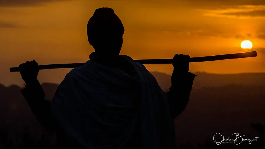 Silhouette d’un homme portant son bâton sur les épaules, face au soleil couchant