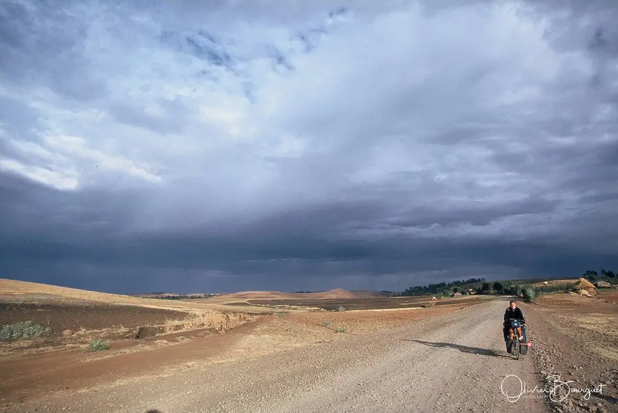 Un cycliste seul sur une piste, sous un grand ciel d’orage, en Éthiopie